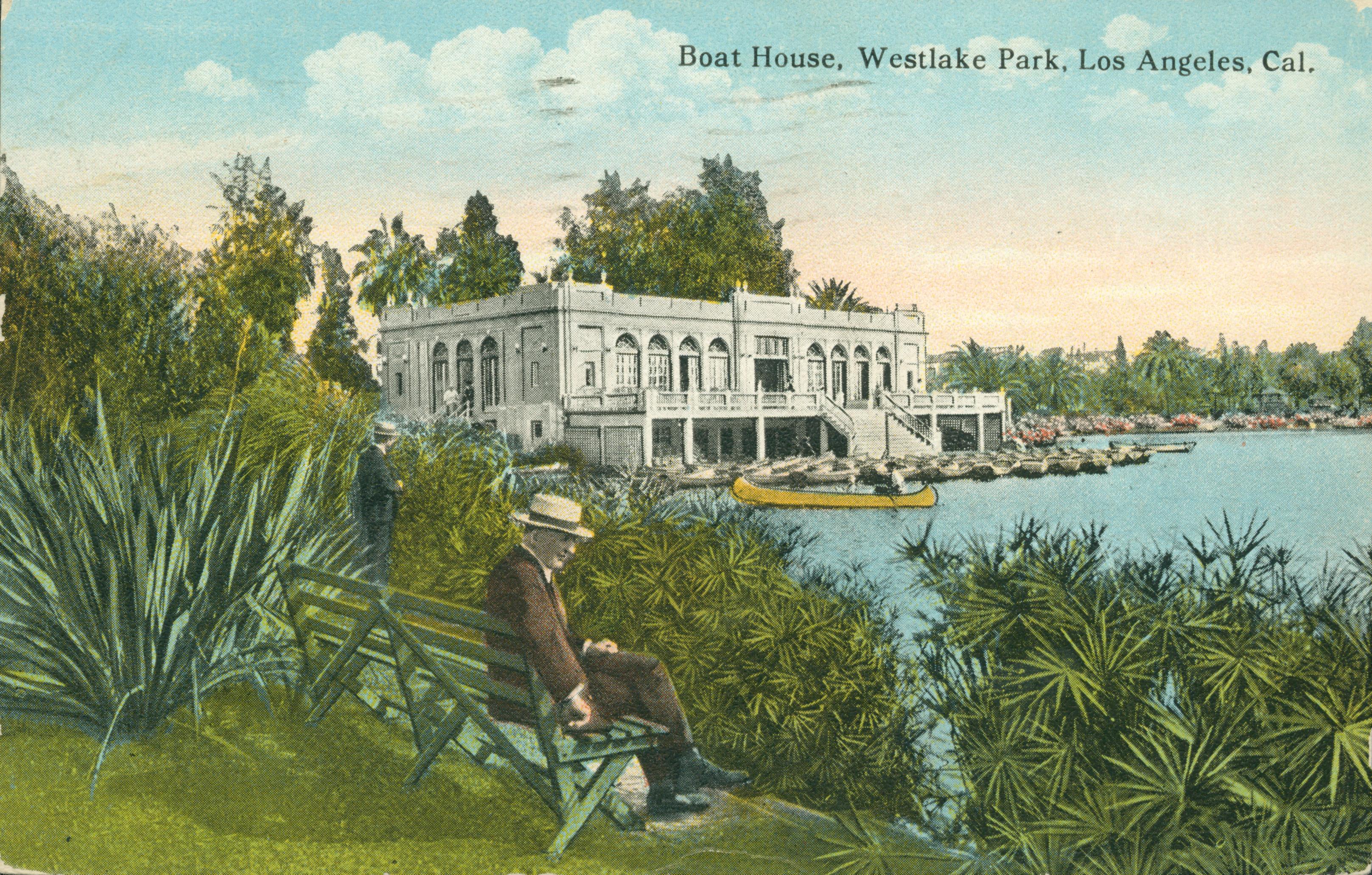 This postcard shows a man seated on a bridge, overlooking a lake, with a boathouse and canoe in the background.